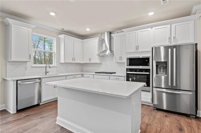 kitchen with wall chimney exhaust hood, a kitchen island, white cabinetry, and stainless steel appliances