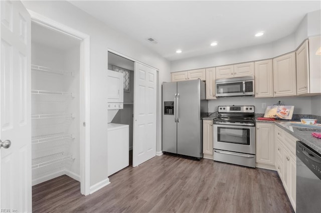 kitchen featuring light hardwood / wood-style floors, stacked washing maching and dryer, appliances with stainless steel finishes, and dark stone counters