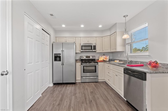 kitchen featuring light stone countertops, hanging light fixtures, appliances with stainless steel finishes, and light hardwood / wood-style flooring