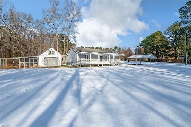 snow covered property featuring an outbuilding, a carport, and a garage