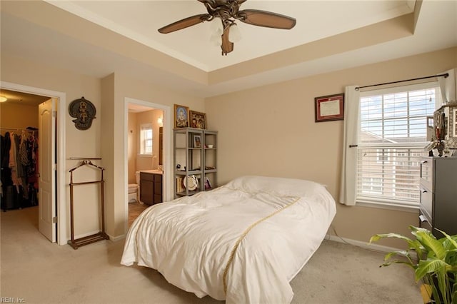 bedroom with ensuite bath, a spacious closet, ceiling fan, a tray ceiling, and a closet