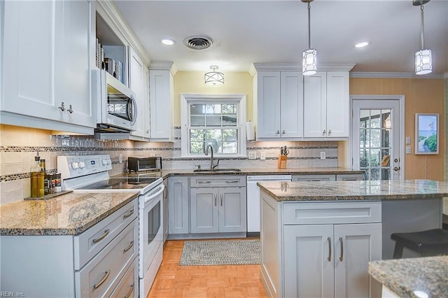 kitchen featuring white appliances, light stone countertops, pendant lighting, light parquet flooring, and sink