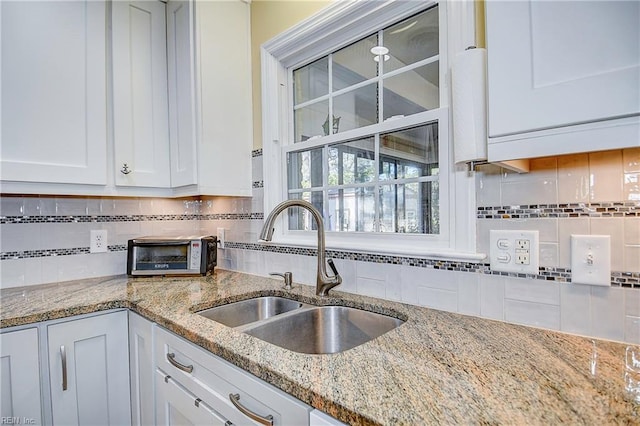 kitchen featuring white cabinets, backsplash, light stone counters, and sink