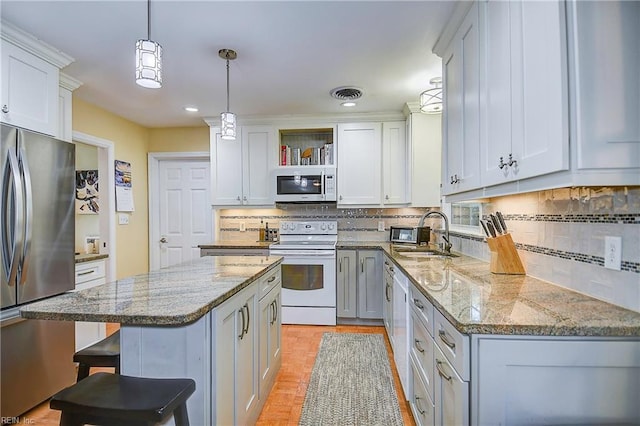 kitchen featuring white appliances, pendant lighting, a kitchen island, white cabinets, and sink