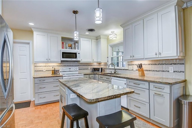 kitchen with white appliances, white cabinets, a kitchen island, and decorative light fixtures