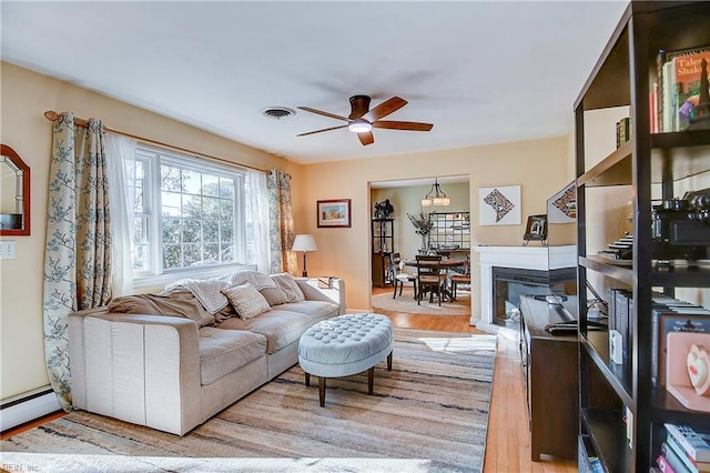 living room featuring baseboard heating, ceiling fan, and light hardwood / wood-style floors