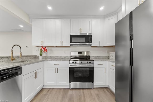 kitchen with white cabinetry, appliances with stainless steel finishes, light stone countertops, sink, and light hardwood / wood-style flooring