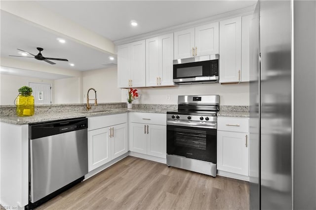 kitchen with appliances with stainless steel finishes, light stone countertops, ceiling fan, white cabinets, and sink