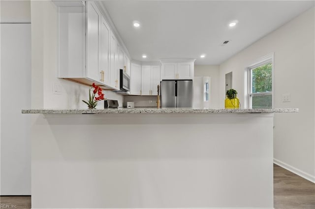 kitchen featuring kitchen peninsula, light stone countertops, stainless steel appliances, hardwood / wood-style floors, and white cabinets