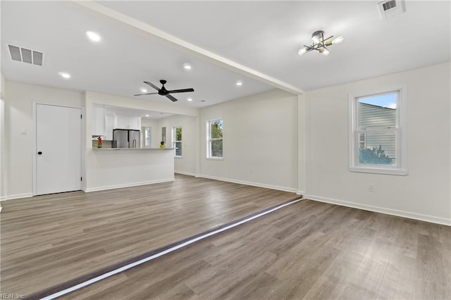 unfurnished living room with ceiling fan with notable chandelier and hardwood / wood-style flooring