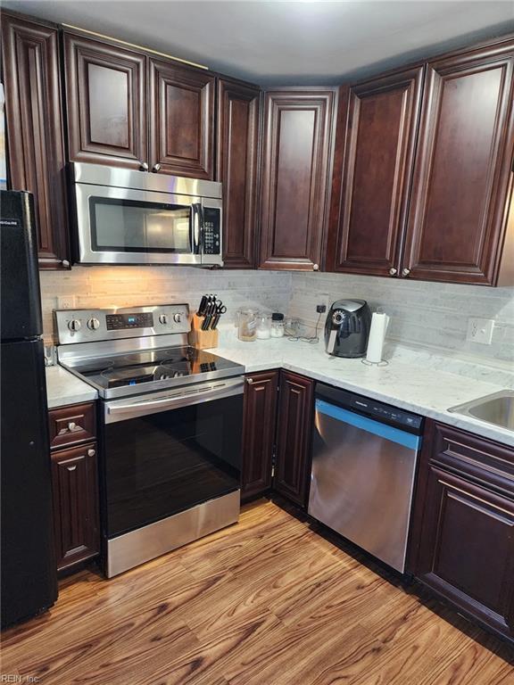 kitchen with appliances with stainless steel finishes, light wood-type flooring, tasteful backsplash, and dark brown cabinetry