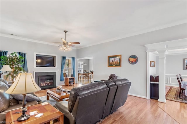 living room featuring ceiling fan, light hardwood / wood-style floors, crown molding, and ornate columns