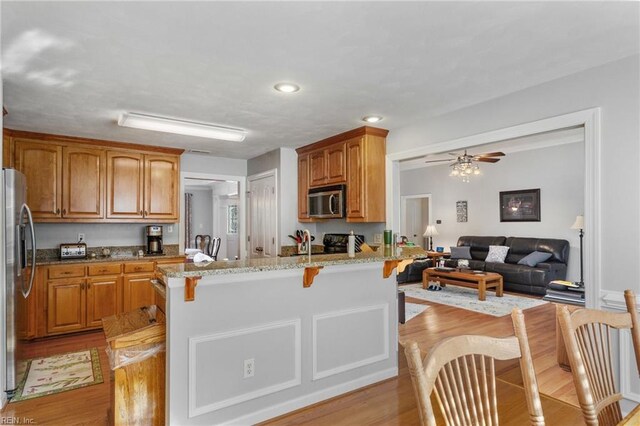 kitchen featuring kitchen peninsula, light wood-type flooring, light stone countertops, a kitchen breakfast bar, and stainless steel appliances