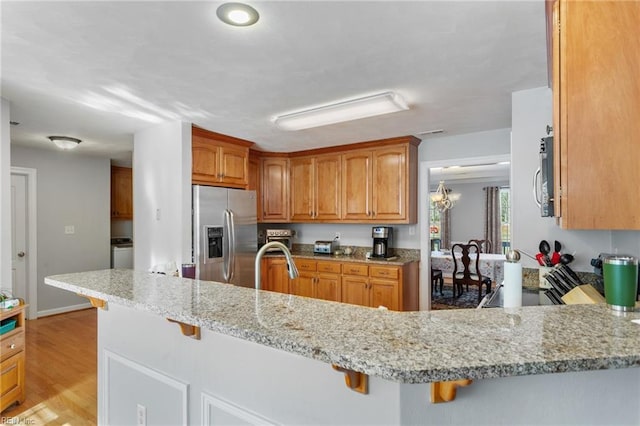 kitchen with light stone counters, a kitchen breakfast bar, appliances with stainless steel finishes, and kitchen peninsula