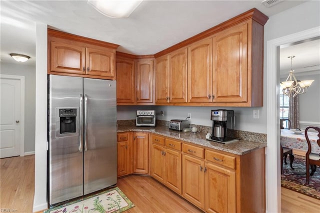 kitchen with stainless steel fridge with ice dispenser, an inviting chandelier, light hardwood / wood-style flooring, and dark stone counters