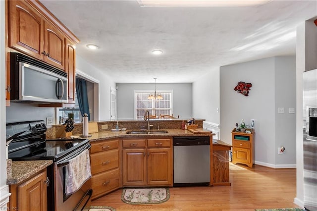 kitchen with decorative light fixtures, light hardwood / wood-style floors, sink, appliances with stainless steel finishes, and dark stone counters