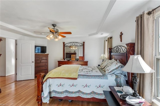 bedroom with ceiling fan, ornamental molding, wood-type flooring, and a tray ceiling