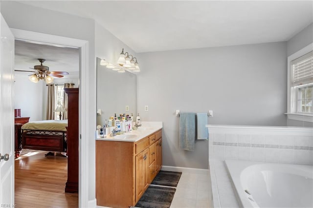 bathroom with ceiling fan, a relaxing tiled tub, and vanity