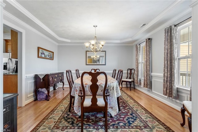 dining area featuring a raised ceiling, light wood-type flooring, a notable chandelier, and crown molding