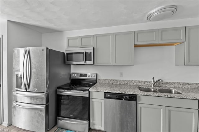 kitchen with gray cabinets, light stone countertops, sink, and stainless steel appliances