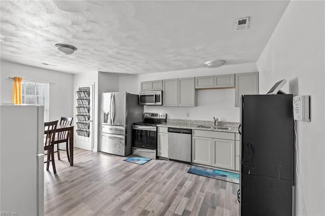 kitchen with light stone countertops, appliances with stainless steel finishes, light wood-type flooring, sink, and gray cabinets