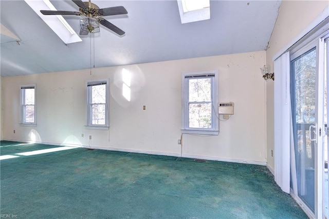 unfurnished room featuring dark colored carpet, ceiling fan, vaulted ceiling with skylight, and a wealth of natural light