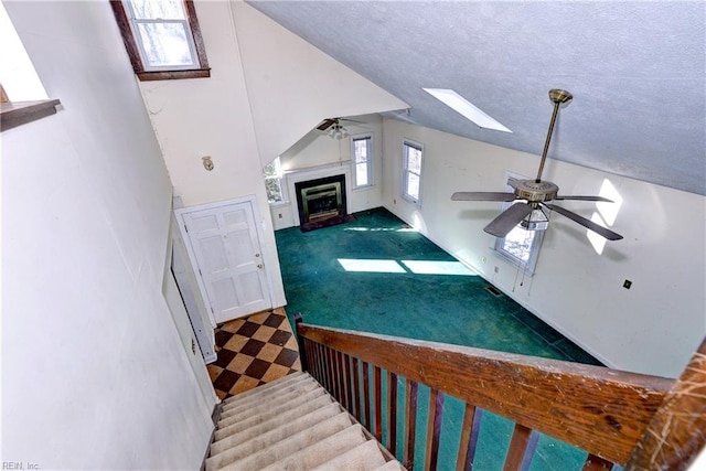 staircase featuring a textured ceiling, carpet floors, ceiling fan, and vaulted ceiling with skylight