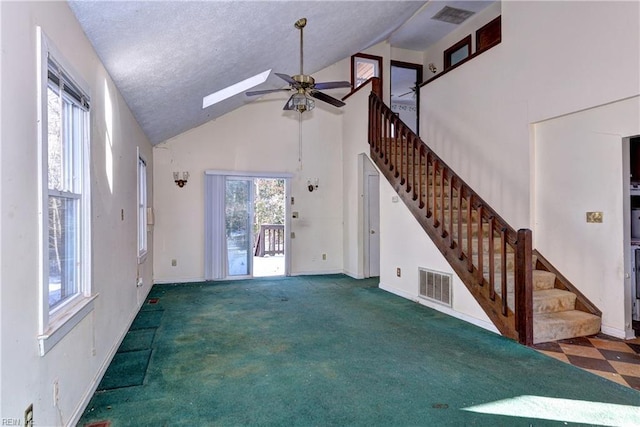 unfurnished living room with high vaulted ceiling, ceiling fan, a skylight, and a healthy amount of sunlight