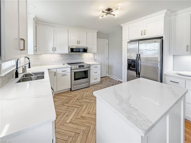 kitchen featuring appliances with stainless steel finishes, light stone counters, sink, white cabinets, and a center island