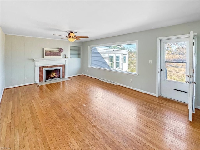 unfurnished living room with a brick fireplace, built in features, ceiling fan, and wood-type flooring