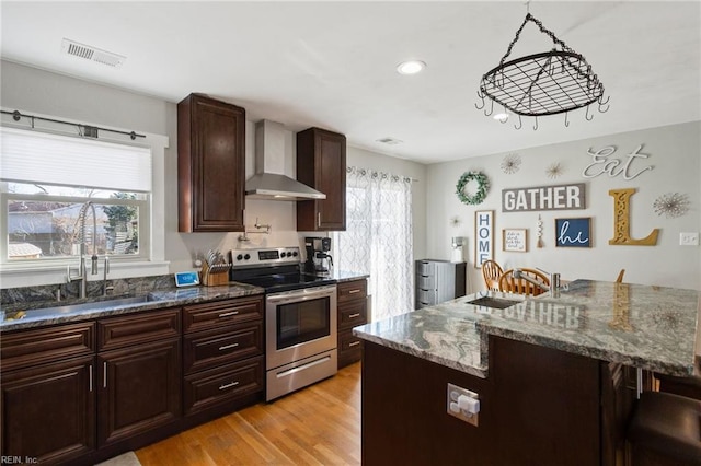 kitchen with wall chimney exhaust hood, pendant lighting, electric range, dark stone counters, and sink