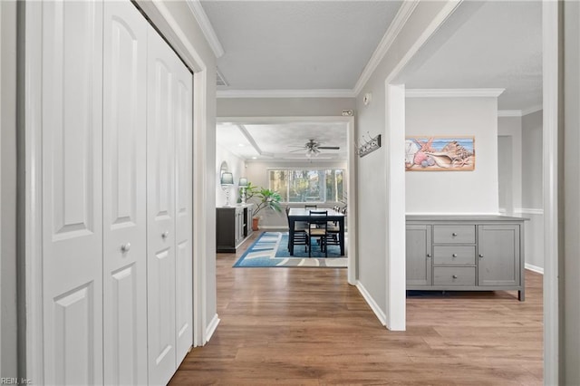 corridor with light wood-type flooring and crown molding