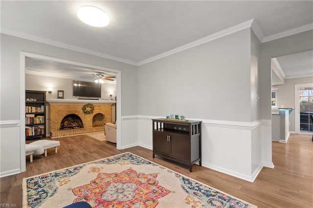 sitting room featuring a brick fireplace, ceiling fan, crown molding, and light hardwood / wood-style flooring