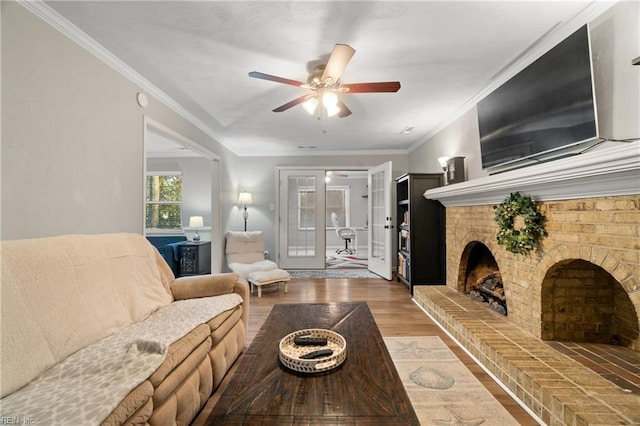 living room with hardwood / wood-style floors, ceiling fan, a brick fireplace, and crown molding