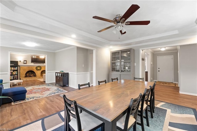 dining space with a brick fireplace, ceiling fan, ornamental molding, and wood-type flooring