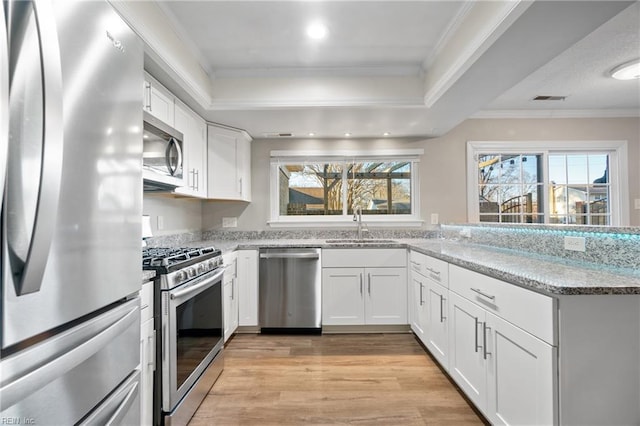 kitchen featuring stainless steel appliances, sink, white cabinetry, light stone counters, and a wealth of natural light