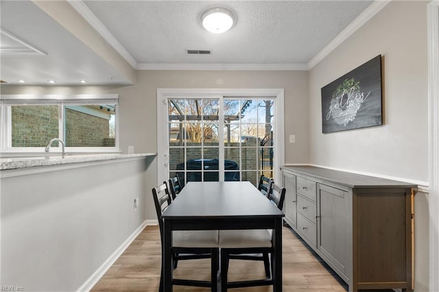 dining room with a textured ceiling, ornamental molding, and light wood-type flooring