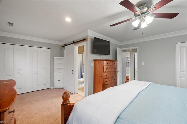 bedroom featuring ceiling fan, ornamental molding, a barn door, and connected bathroom