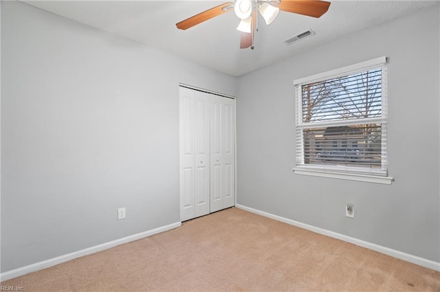 unfurnished bedroom featuring ceiling fan, light colored carpet, and a closet