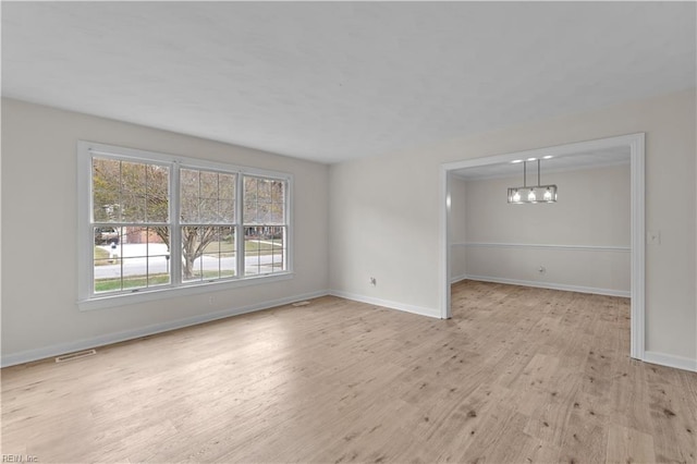 empty room featuring an inviting chandelier and light hardwood / wood-style flooring