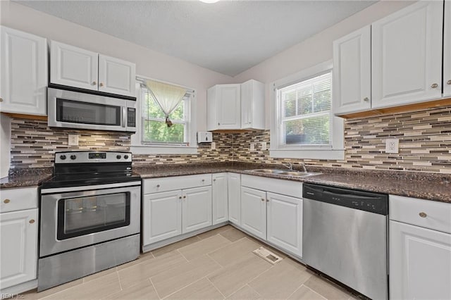 kitchen with backsplash, sink, appliances with stainless steel finishes, light tile patterned flooring, and white cabinetry