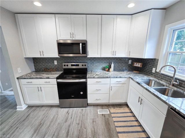 kitchen featuring white cabinets, appliances with stainless steel finishes, sink, light wood-type flooring, and light stone counters