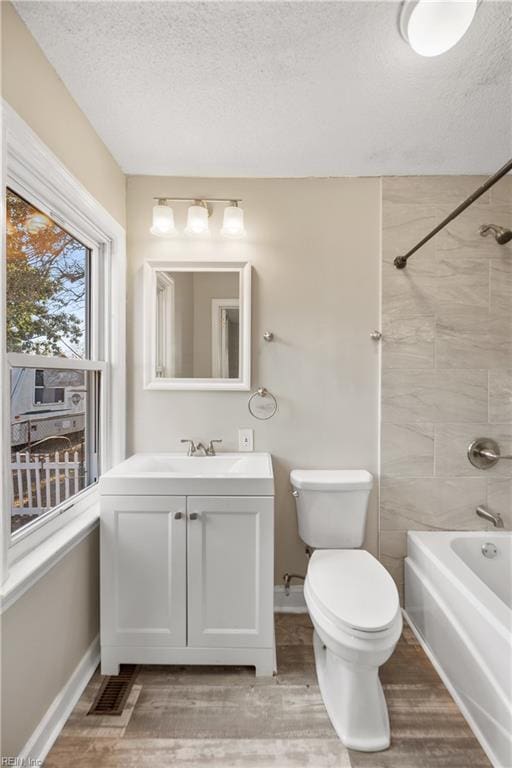 full bathroom with vanity, a textured ceiling, tiled shower / bath combo, hardwood / wood-style floors, and toilet