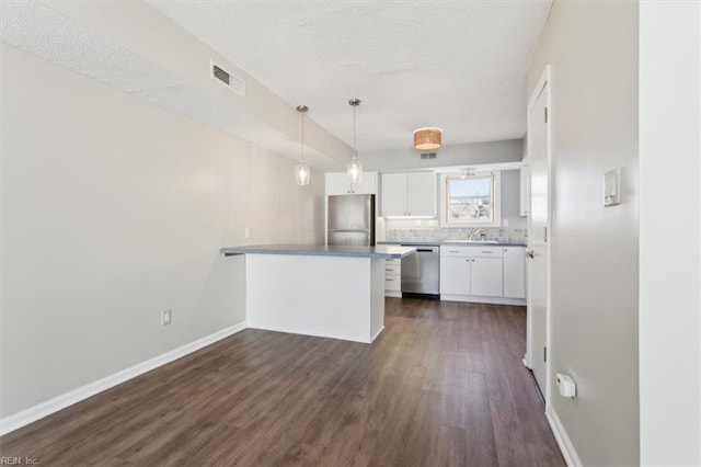 kitchen with kitchen peninsula, hanging light fixtures, decorative backsplash, white cabinetry, and appliances with stainless steel finishes