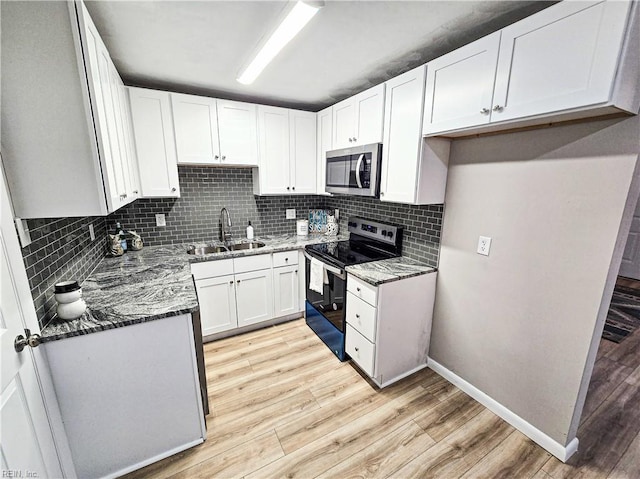 kitchen featuring white cabinets, appliances with stainless steel finishes, dark stone counters, light hardwood / wood-style floors, and sink