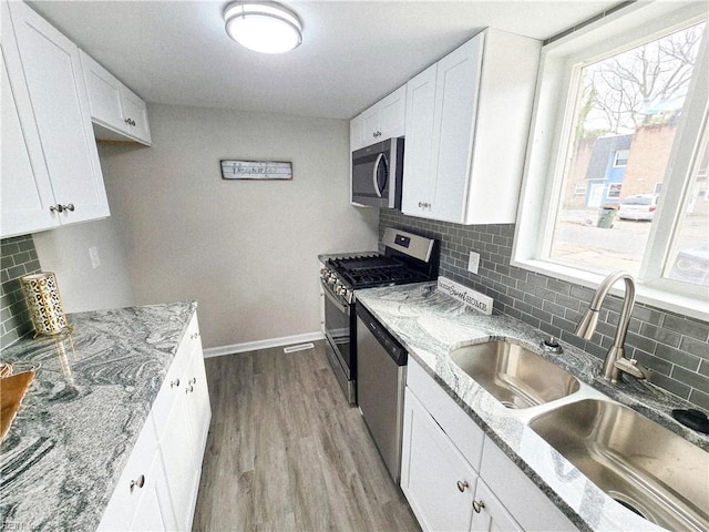 kitchen featuring stainless steel appliances, white cabinetry, sink, and light stone countertops