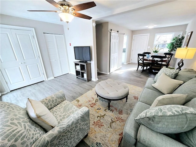 living room featuring ceiling fan, light hardwood / wood-style floors, and a barn door