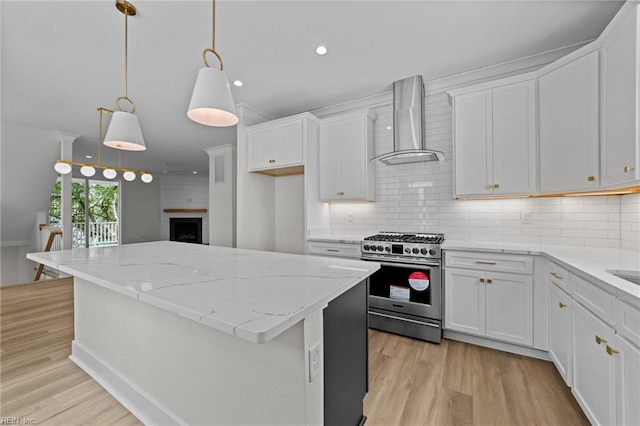 kitchen featuring decorative light fixtures, backsplash, white cabinets, wall chimney exhaust hood, and gas range