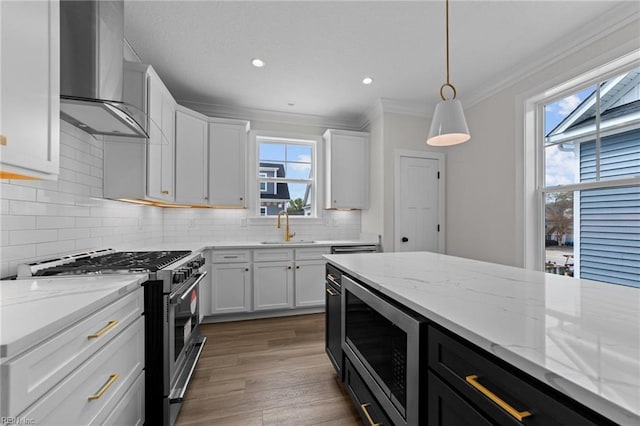 kitchen with white cabinets, appliances with stainless steel finishes, wall chimney exhaust hood, decorative light fixtures, and a healthy amount of sunlight