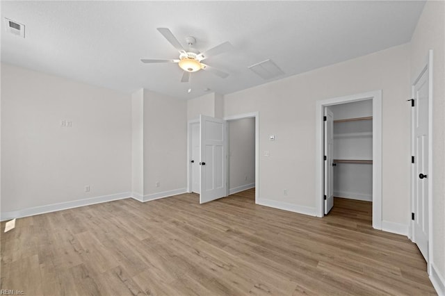 unfurnished bedroom featuring ceiling fan, a walk in closet, a closet, and light hardwood / wood-style floors